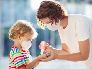 Woman giving child hand sanitizer as part of COVID-19 precautions